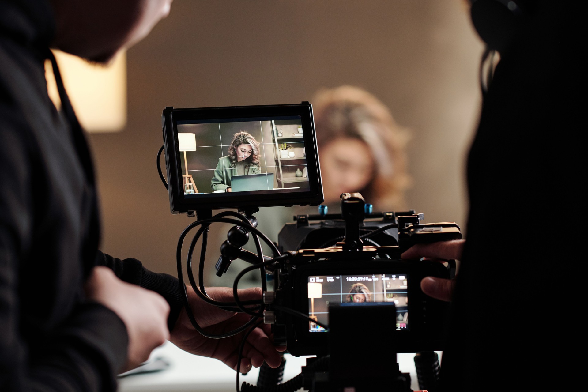 Close-up of steadicam screens with female model using laptop by table